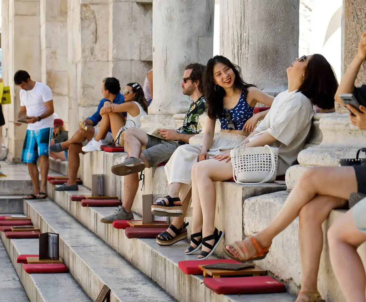 Guests sitting on Lvxor's red cushions on the ancient steps of Peristil Square in Split